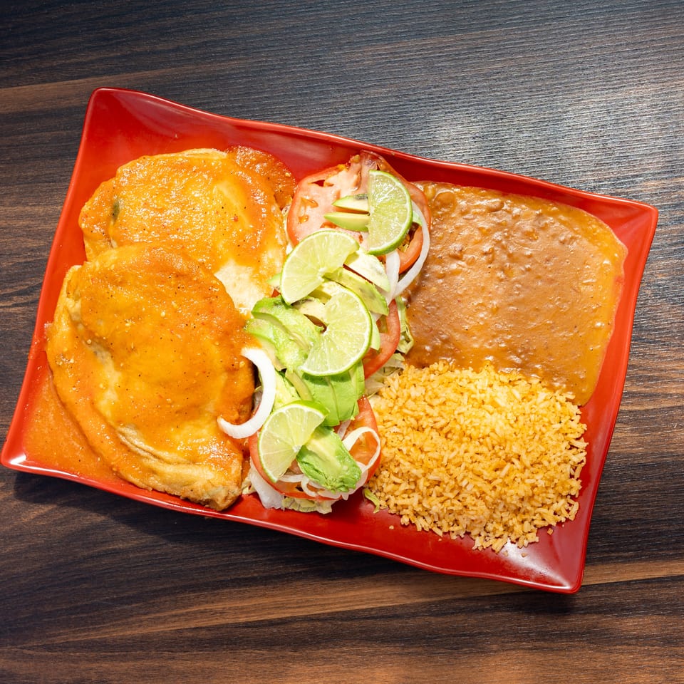 Mexican plate with enchiladas, refried beans, rice, and salad topped with avocado and lime wedges.