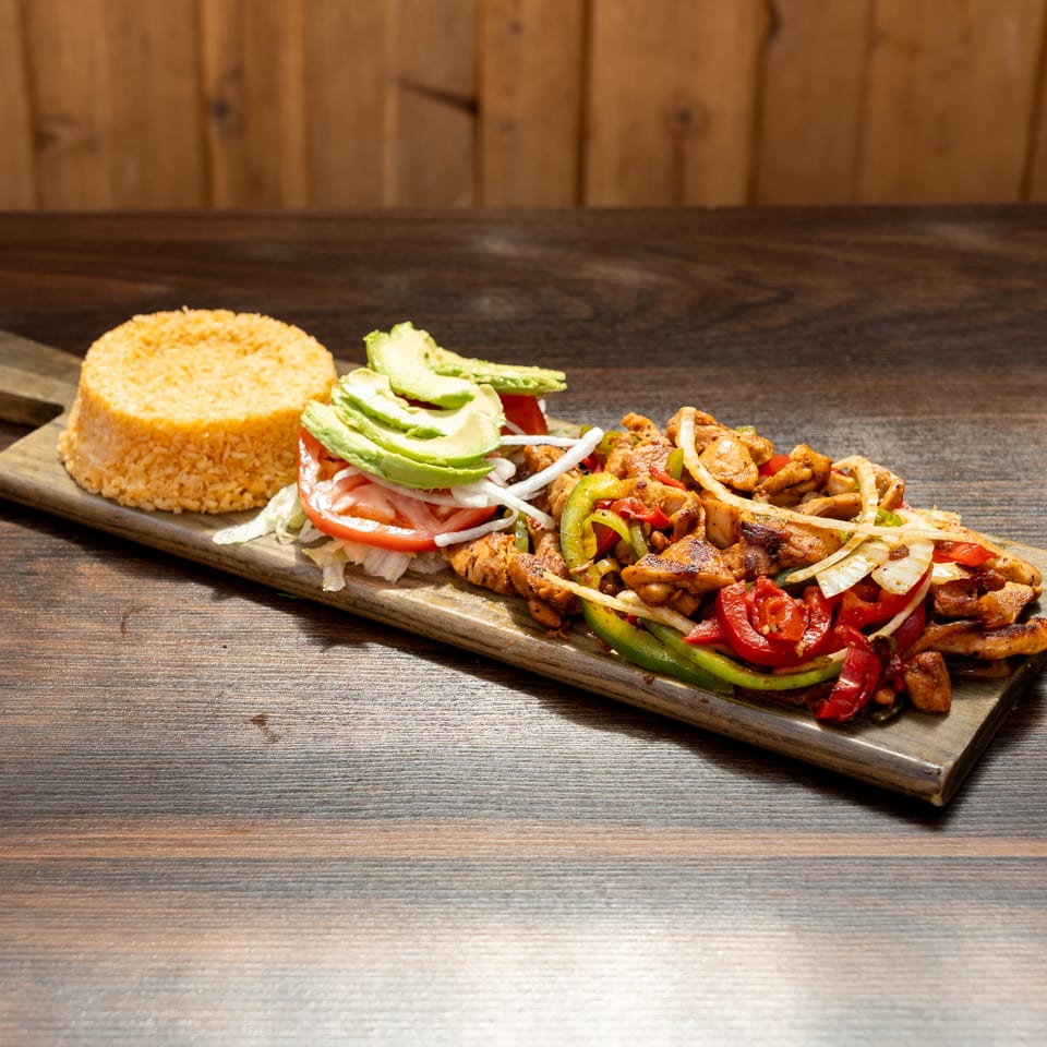 Grilled chicken with peppers, onions, tomatoes, avocado, and rice served on a wooden platter.