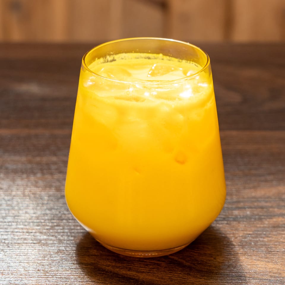 Bright orange beverage with ice fills a rounded glass on a wooden restaurant table.