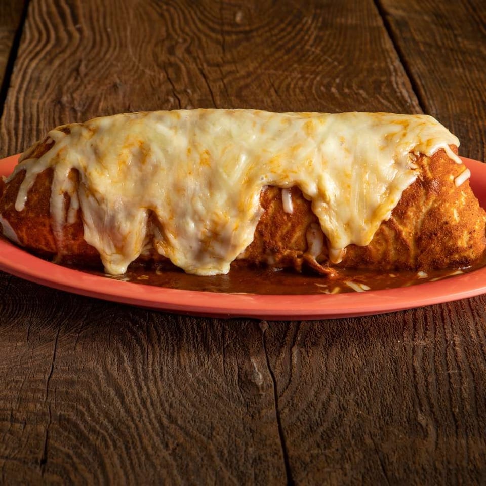 Golden-brown enchiladas covered in melted cheese and red sauce, served on an orange plate atop a rustic wooden table.