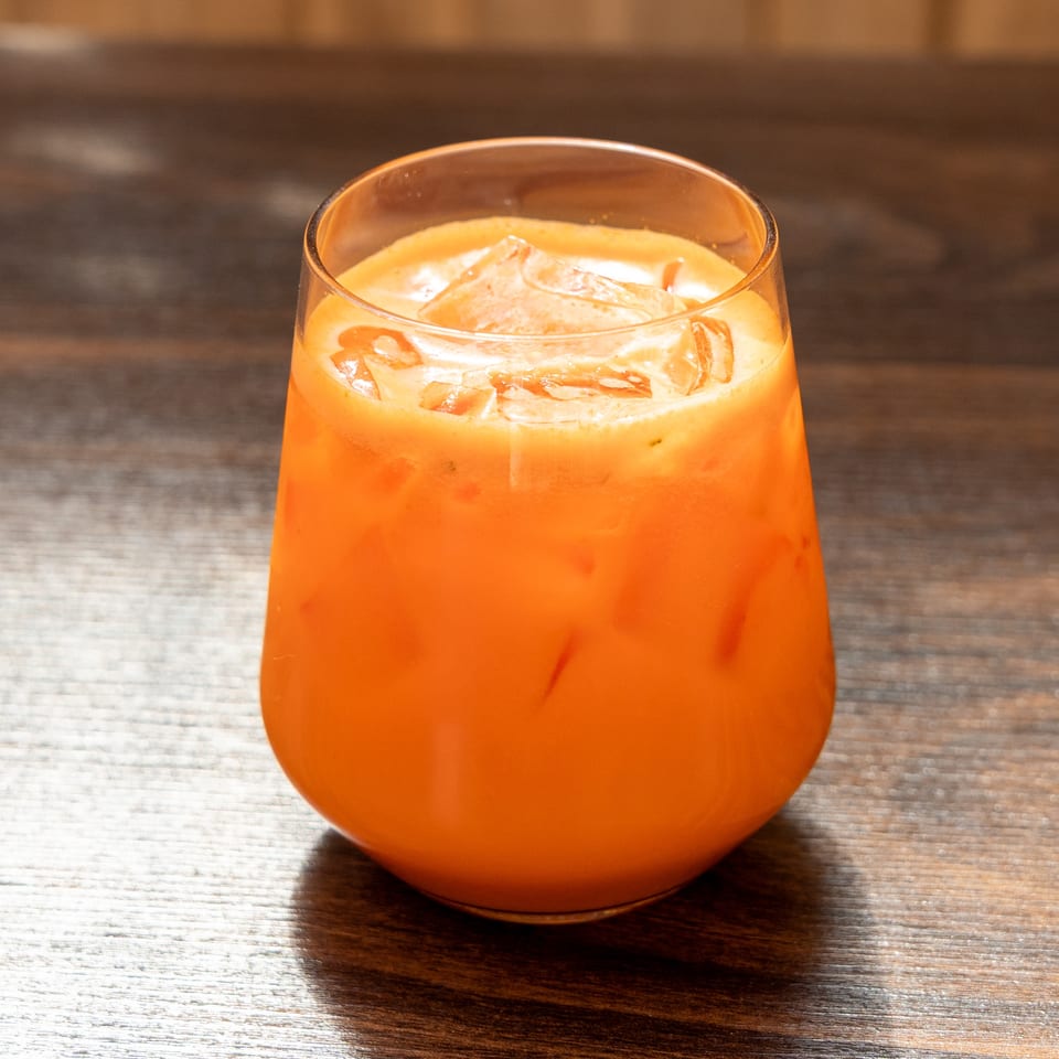 Bright orange cocktail with ice in a rounded glass on a wooden bar.