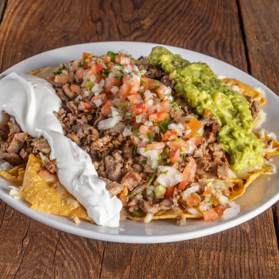 Loaded nachos topped with seasoned meat, pico de gallo, guacamole, sour cream, and melted cheese on a white plate.