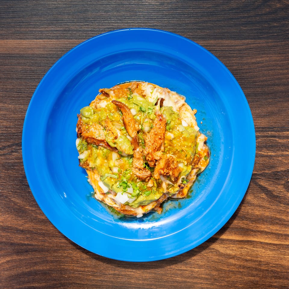 Loaded Mexican-style dish topped with grilled chicken, guacamole, melted cheese, onions, and cilantro on a bright blue plate.