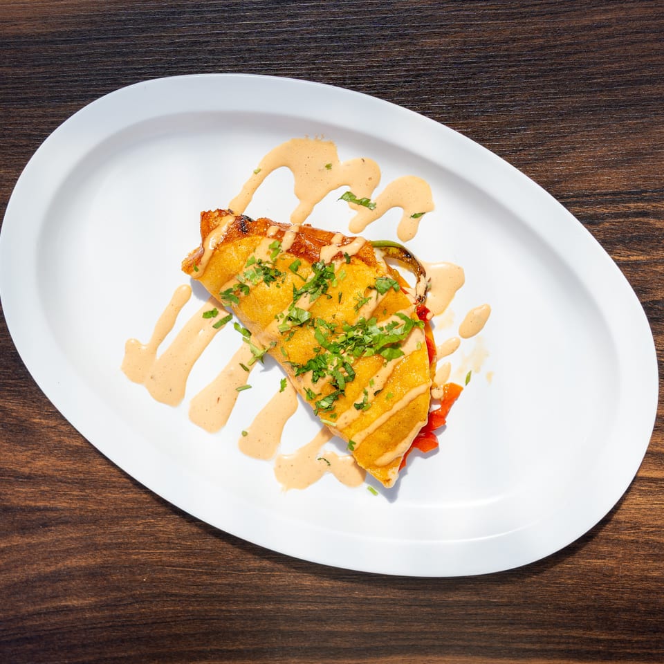 Golden-brown stuffed entrée topped with chopped herbs and creamy sauce on a white plate over a wooden table.