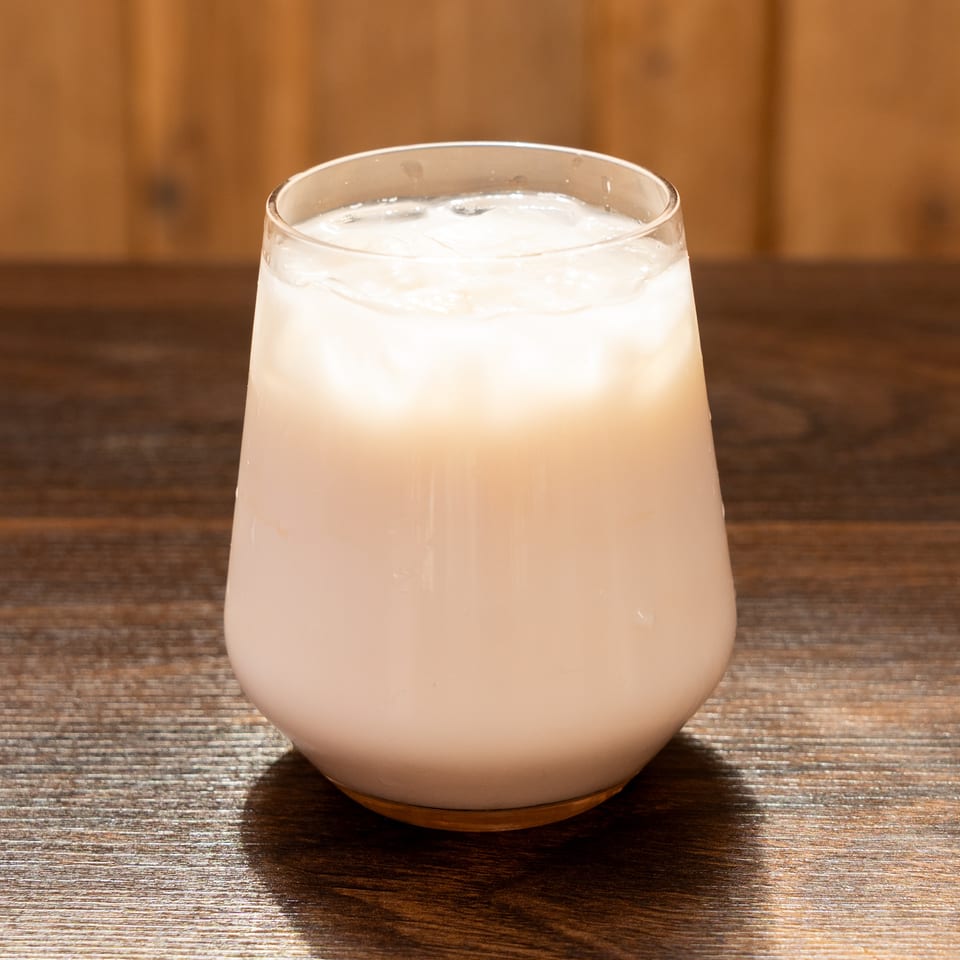 Creamy pale cocktail with ice served in a rounded glass on a wooden restaurant table.