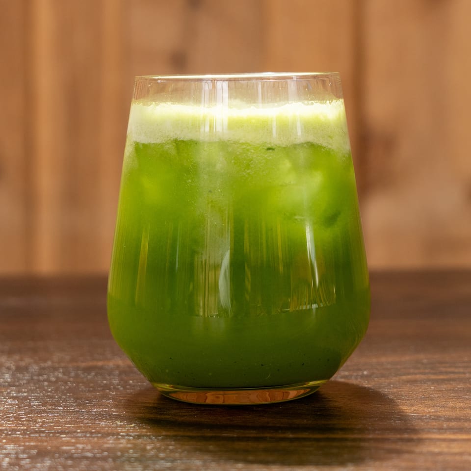 Bright green frothy beverage served in a rounded glass on a wooden table.